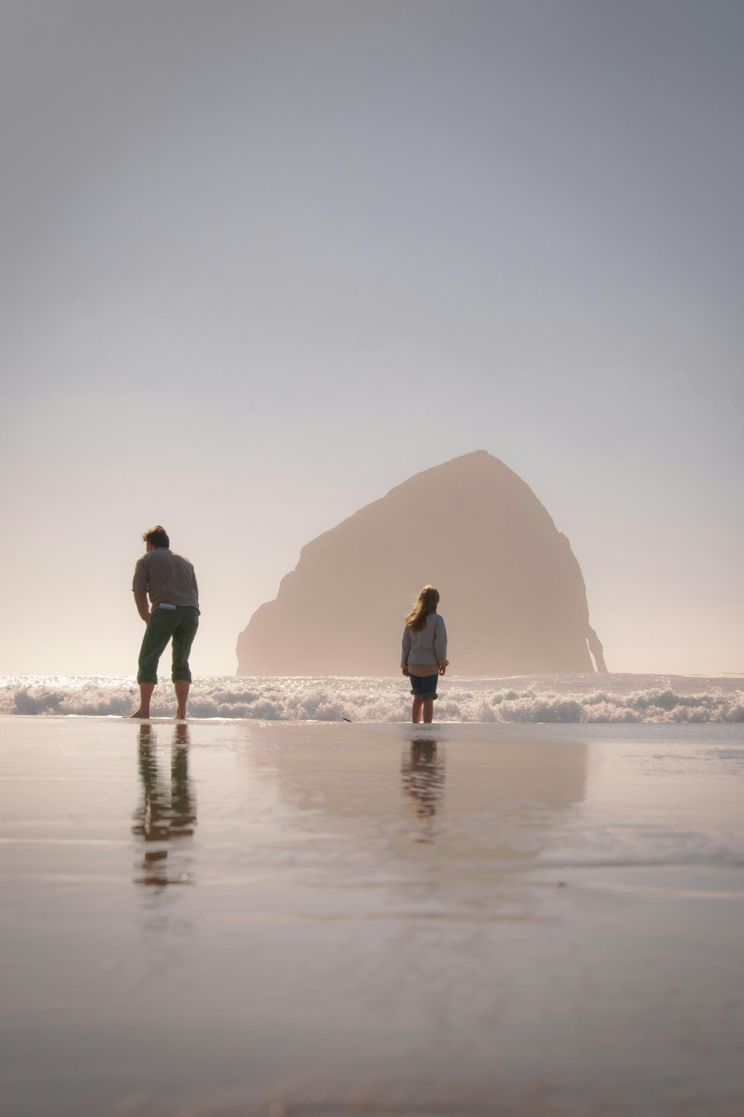 2 people standing on the short, facing small waves, dusk. Photo by Marshall Iden - Unsplash