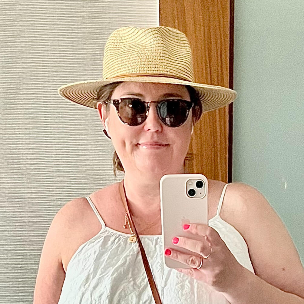 Portrait of Lauren, wearing a wide-brimmed hat and sunglasses, smiling warmly.