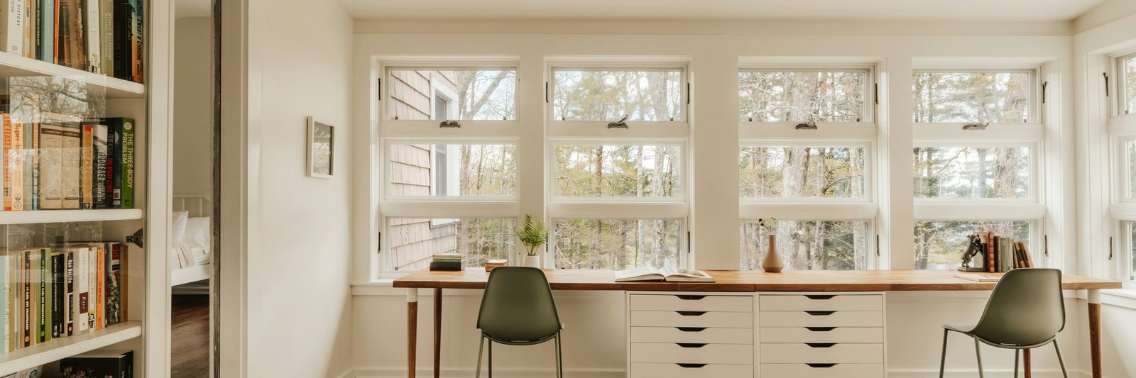 A bright room lined with bookshelves full of books beside sunlit windows.